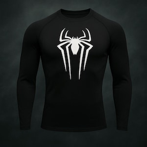Puede incluir: Camiseta negra de manga larga con un emblema de araña blanco en el pecho. El emblema es una araña estilizada con líneas afiladas y angulares. La camiseta tiene cuello redondo y está hecha de un material liso, probablemente atlético.