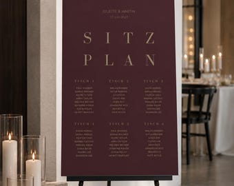 May include: A dark burgundy wedding seating chart sign on a black easel. The sign features the text JULIETTE & MARTIN, 07 JULI 2027, and SITZ PLAN in gold lettering, followed by six tables with lists of names printed in a clean, sans-serif font.