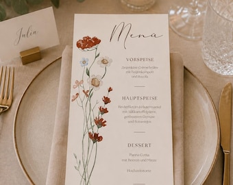 May include: A vertical rectangular menu card printed on white paper featuring a watercolor illustration of wildflowers in red, blue, and pink. The text includes the word Menü, course headings, food descriptions, and the names Julia & David with the date.