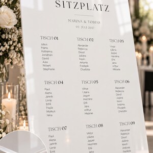 May include: A white acrylic wedding seating chart sign featuring the text "finde deinen SITZPLATZ", "MARINA & TOBIAS", and "07. JULI 2027" with lists of names organized by table numbers. A circular inset shows the 5 mm thick acrylic material.