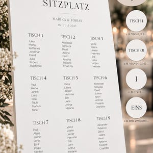 May include: A white wedding seating chart sign on a black easel featuring the text 'finde deinen SITZPLATZ', 'MARINA & TOBIAS', '07. JULI 2027', and lists of names under tables 1 through 9. Circular callouts show alternative table numbering styles.