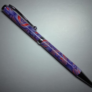 Könnte beinhalten: Ein lila und roter marmorierter Stift mit silberner Klammer und Spitze.