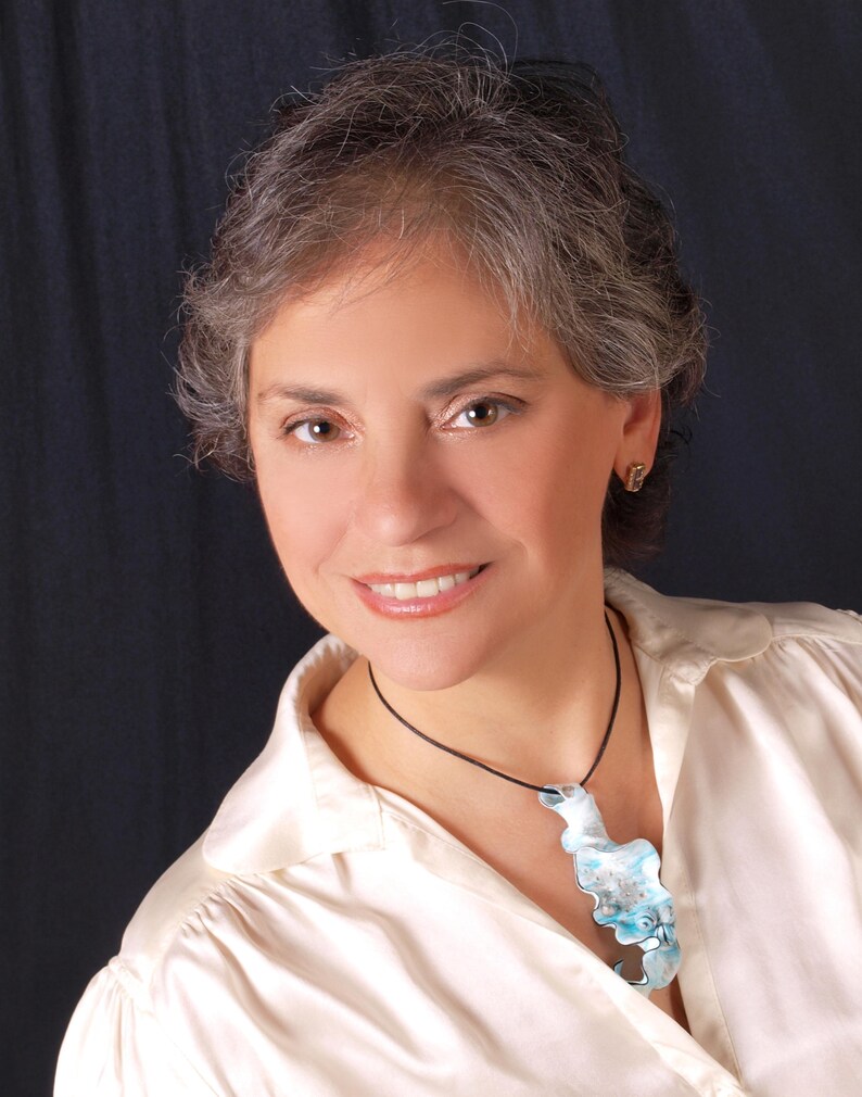 May include: A woman with grey hair is wearing a white blouse with a blue and white glass pendant necklace.