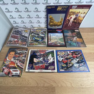 May include: A collection of ten vintage NASCAR and Indianapolis 500 racing event programs. The booklets feature various race car graphics, driver portraits, and promotional imagery, including a cover with Batman and Joker illustrations.