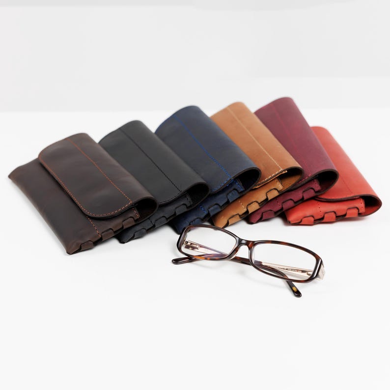 Pode incluir: Uma cole&ccedil;&atilde;o de estojos de &oacute;culos de couro em v&aacute;rias cores, incluindo castanho, preto, azul marinho, bege, bord&ocirc; e vermelho. Um par de &oacute;culos com arma&ccedil;&atilde;o tartaruga est&aacute; em frente aos estojos.