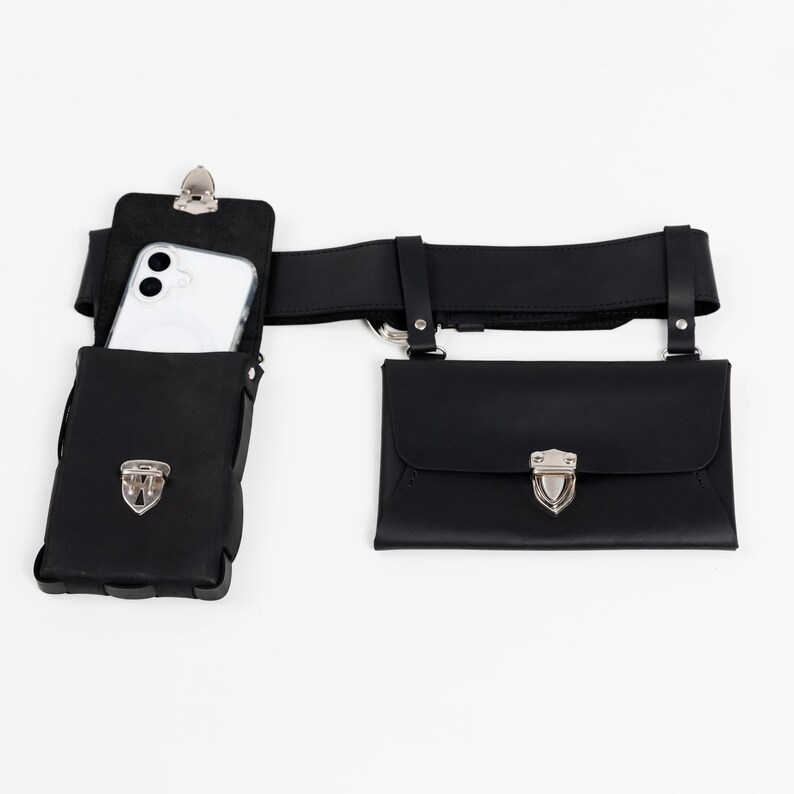 May include: Black leather belt bag with two pouches and a phone holder. The phone holder has a silver clip and holds a white smartphone. The pouches have silver clasps. The belt is black and has silver hardware.