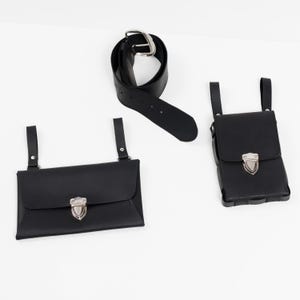 May include: A black leather belt with a silver buckle, and two black leather pouches with silver clasps. One pouch is rectangular, the other is square. The pouches have straps for attaching to a belt.