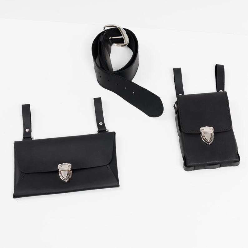 May include: A black leather belt with a silver buckle, and two black leather pouches with silver clasps. One pouch is rectangular, the other is square. The pouches have straps for attaching to a belt.