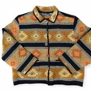 May include: A patterned button-down jacket. The jacket features a repeating geometric design in shades of orange, tan, and black. The sleeves and collar are trimmed with black fabric. The jacket has four buttons. The style is reminiscent of the American Southwest.
