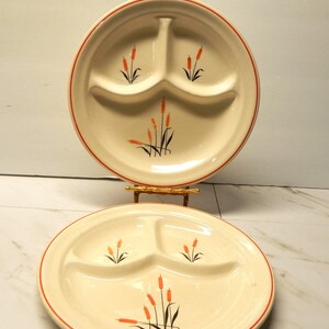 May include: Two cream-colored ceramic divided plates featuring three sections each. The plates are decorated with a painted cattail motif in orange and black, and each plate is finished with a thin orange rim around the outer edge.
