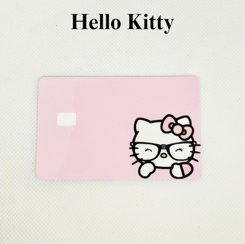 Pu&ograve; includere: Una carta rosa con le parole "Hello Kitty" in alto. La carta presenta una grafica di Hello Kitty con occhiali e un fiocco. La carta ha un quadrato bianco sul lato sinistro.