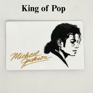 Pu&ograve; includere: Carta rettangolare bianca con un profilo in bianco e nero di Michael Jackson e la sua firma in oro. Il testo "King of Pop" &egrave; sopra l'immagine.