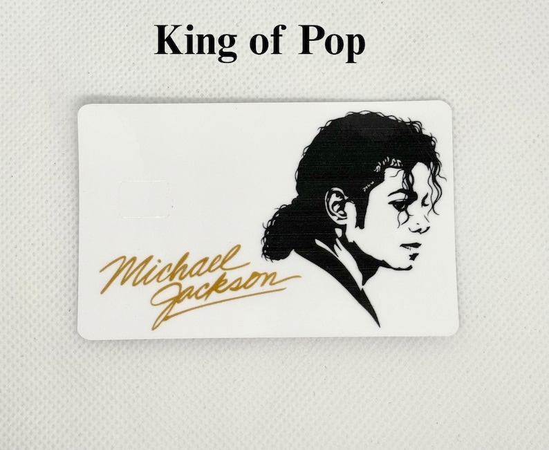 Pu&ograve; includere: Carta rettangolare bianca con un profilo in bianco e nero di Michael Jackson e la sua firma in oro. Il testo "King of Pop" &egrave; sopra l'immagine.