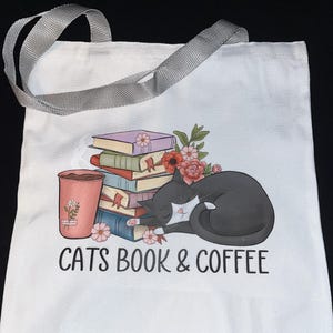 May include: White tote bag with gray handles featuring a graphic of a sleeping black cat, a stack of books, a coffee cup, and the text "CATS BOOK & COFFEE". The books are in various colors, and the coffee cup has a floral design.