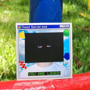 May include: A white sticker with the text "Dead Server.exe" at the top, and "YOU ARE LOVED!" at the bottom. The sticker features a black rectangle with two eyes, and a background of a blue sky with clouds.