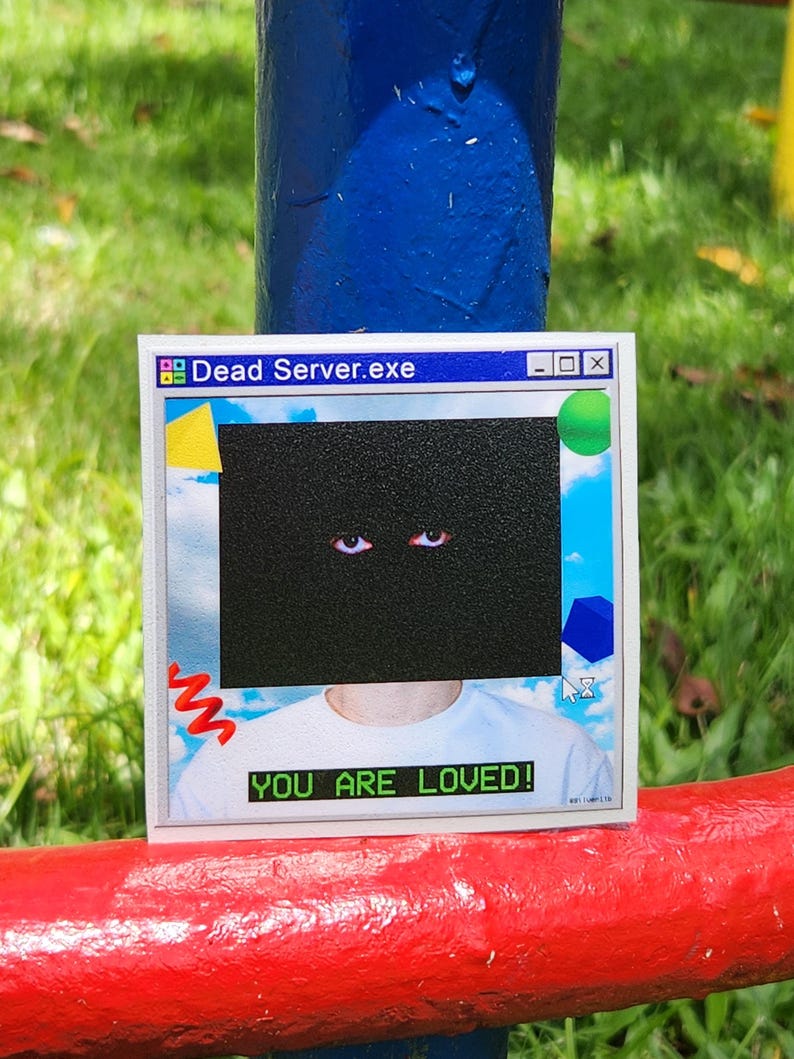 May include: A white sticker with the text "Dead Server.exe" at the top, and "YOU ARE LOVED!" at the bottom. The sticker features a black rectangle with two eyes, and a background of a blue sky with clouds.