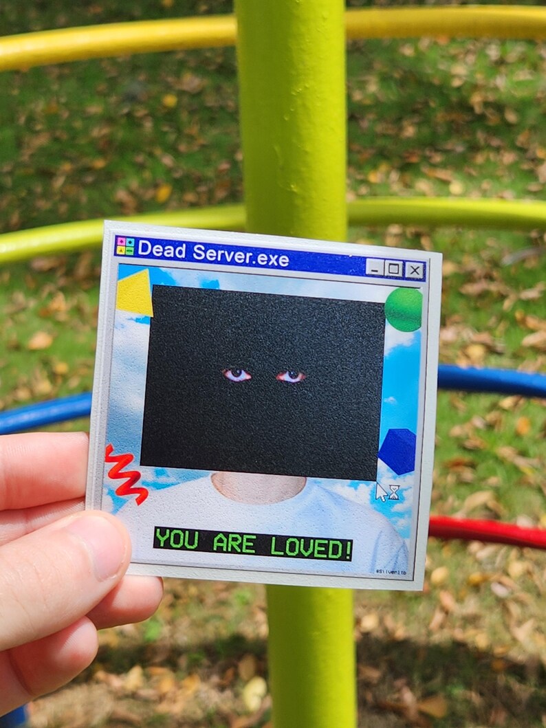 May include: A sticker with a retro computer interface design. The sticker features the text "Dead Server.exe" at the top and "YOU ARE LOVED!" at the bottom. The central graphic is a black box with two red eyes.