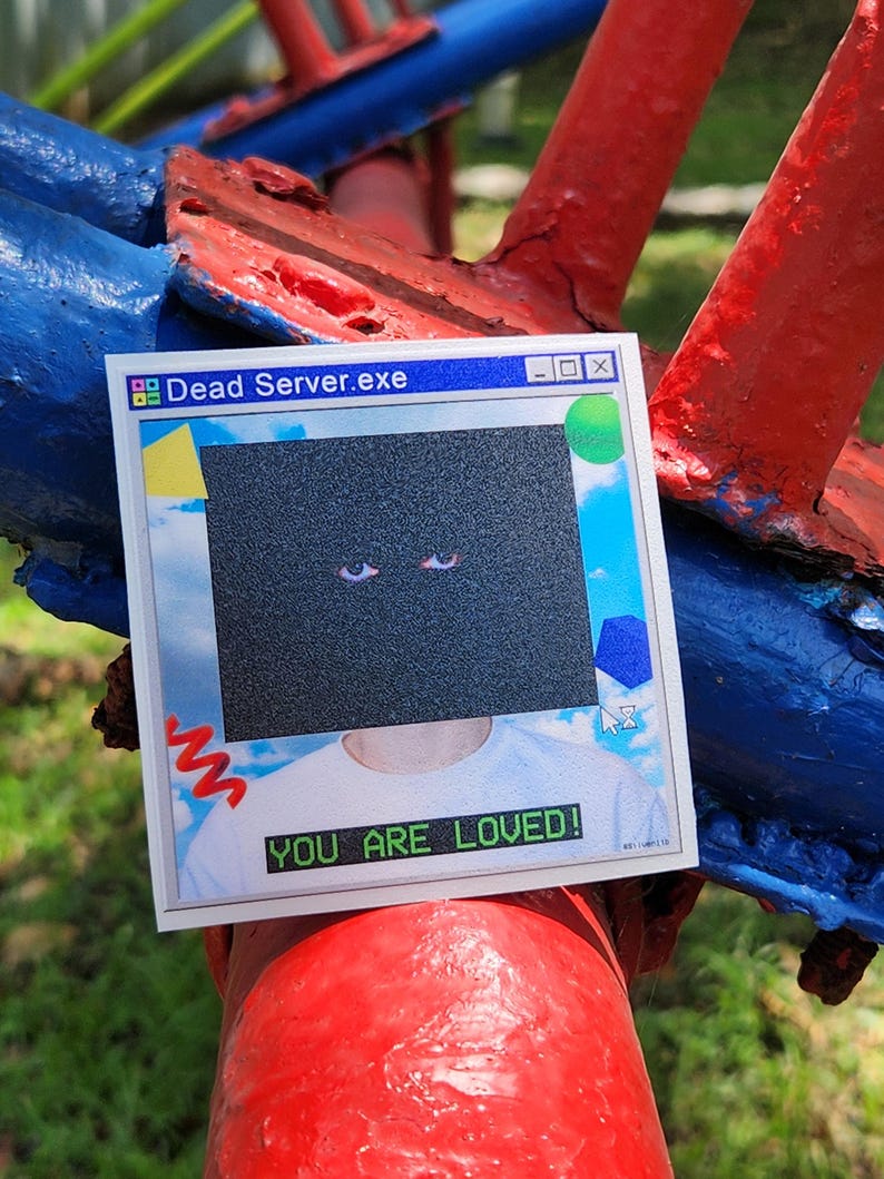 May include: A sticker with a retro computer window design. The text "Dead Server.exe" is at the top, and "YOU ARE LOVED!" is at the bottom. The sticker has a black square with two eyes.