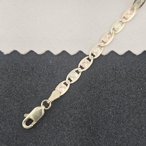 May include: A multi-tone gold chain bracelet featuring a series of oval-shaped links. Each link contains a textured, diamond-cut square center panel alternating between yellow and rose gold tones. The bracelet includes a secure lobster claw clasp.