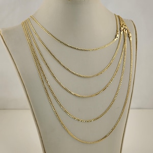 May include: A display of multiple gold-colored chain necklaces of varying lengths. The chains are draped on a mannequin, showcasing their different styles and textures. The necklaces appear to be made of a shiny, metallic material.