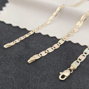 May include: A tri-color gold chain necklace featuring alternating oval links in yellow, white, and rose gold tones. The links have a textured, starburst-like pattern on their surfaces. The chain includes a secure lobster claw clasp closure.