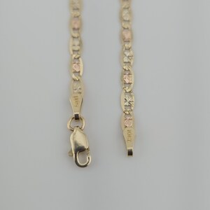 May include: A gold chain necklace featuring alternating oval links with a textured, faceted finish and smooth rose gold accents. The chain includes a lobster claw clasp and a metal tag stamped with the text 10KT, indicating the gold purity.