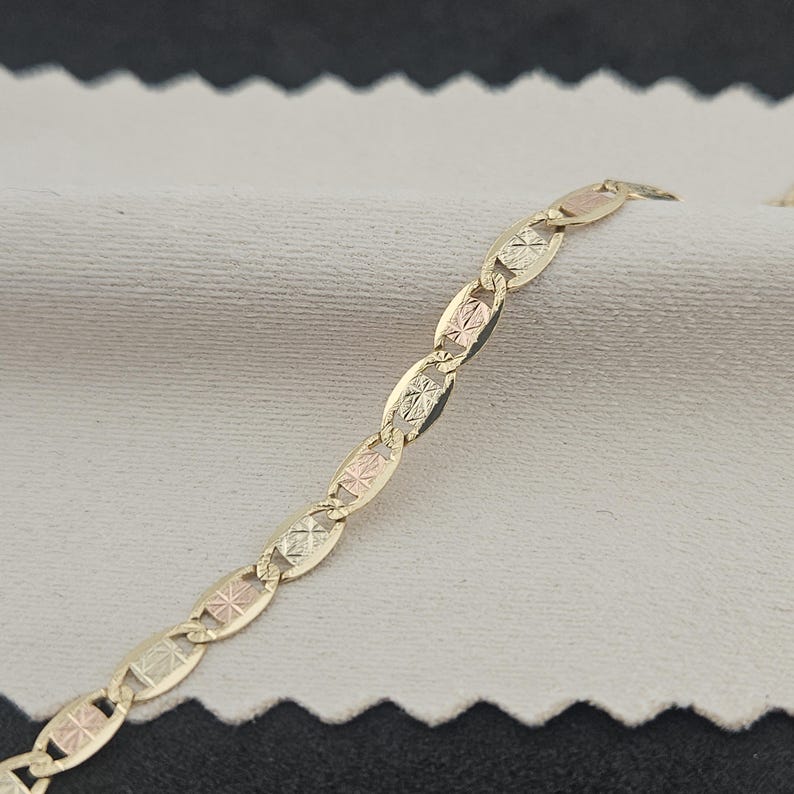 May include: A gold chain necklace featuring a series of oval-shaped links. Each link is constructed with a textured, diamond-cut center panel that displays a subtle tri-color effect, alternating between yellow, rose, and white gold tones.