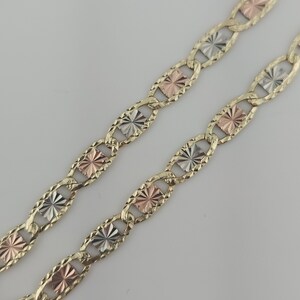 May include: A tri-color gold chain necklace featuring oval links with a textured finish. The chain alternates between yellow gold, rose gold, and white gold rectangular inserts, each displaying a sunburst pattern etched into the metal surface.