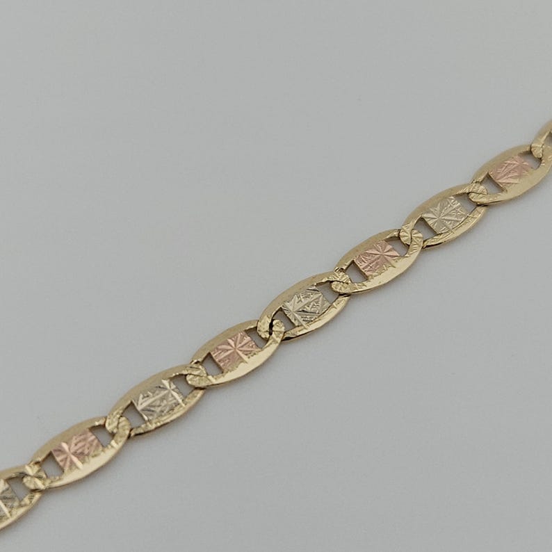 May include: A tri-color gold chain necklace featuring a series of interlocking oval links. Each link is crafted from yellow gold and contains a central square-shaped insert with a textured, diamond-cut finish in alternating rose and white gold.