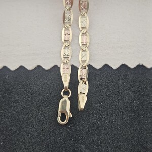 May include: A gold chain necklace featuring alternating oval and rectangular links with a textured, star-like pattern on the surface. The chain includes a lobster claw clasp and is marked with the text GMI and 10KT on the metal components.