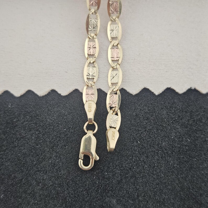 May include: A gold chain necklace featuring alternating oval and rectangular links with a textured, star-like pattern on the surface. The chain includes a lobster claw clasp and is marked with the text GMI and 10KT on the metal components.