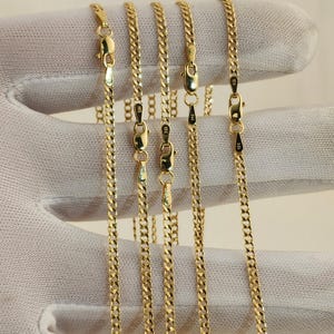 May include: Close-up of several gold-colored curb chain necklaces. Each chain has a lobster clasp closure. The chains are displayed against a white background. The chains are likely made of gold.