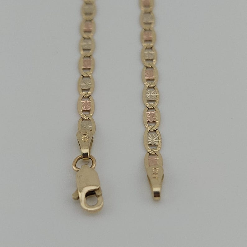May include: A tri-color gold chain necklace featuring alternating oval links with textured starburst patterns in yellow, rose, and white gold tones. The chain includes a lobster claw clasp and a small metal tag stamped with the number 585.