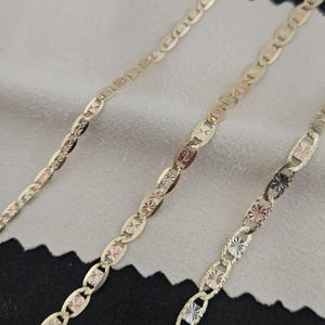 May include: A tri-color gold chain necklace featuring alternating oval links with a polished finish and textured, star-patterned accents in yellow, rose, and white gold tones. The chain displays a repeating pattern of interconnected metal links.