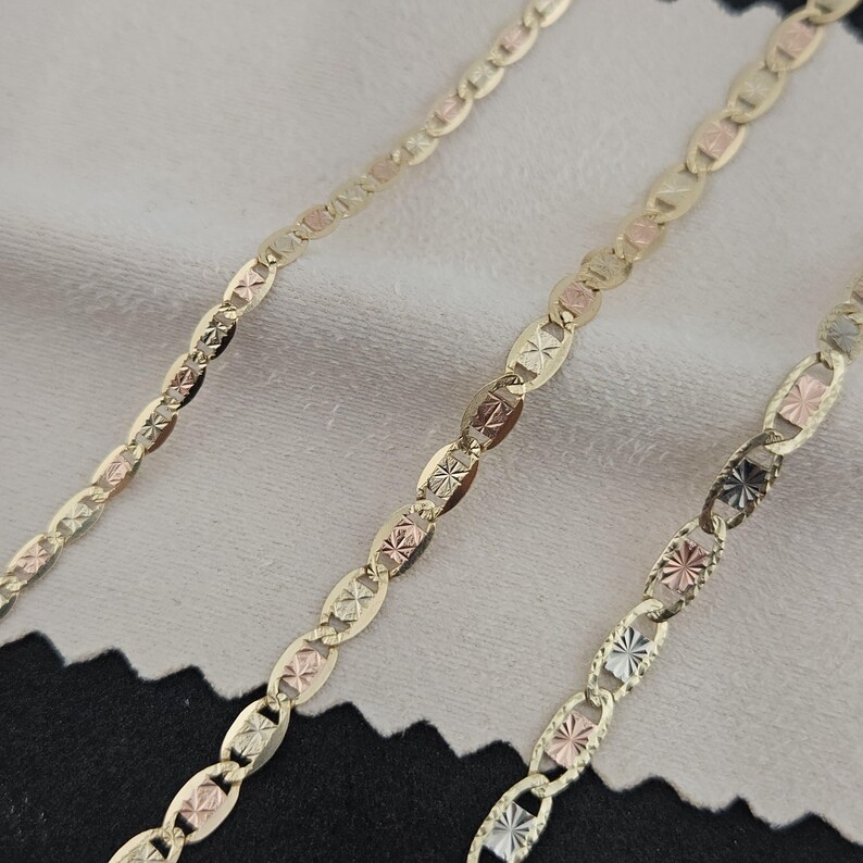 May include: A tri-color gold chain necklace featuring alternating oval links with a polished finish and textured, star-patterned accents in yellow, rose, and white gold tones. The chain displays a repeating pattern of interconnected metal links.