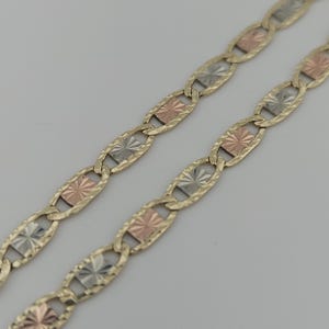 May include: A tri-color chain necklace featuring alternating oval links with a textured finish. The links are connected by small rectangular plates in alternating rose gold, yellow gold, and silver tones, each featuring a sunburst pattern.