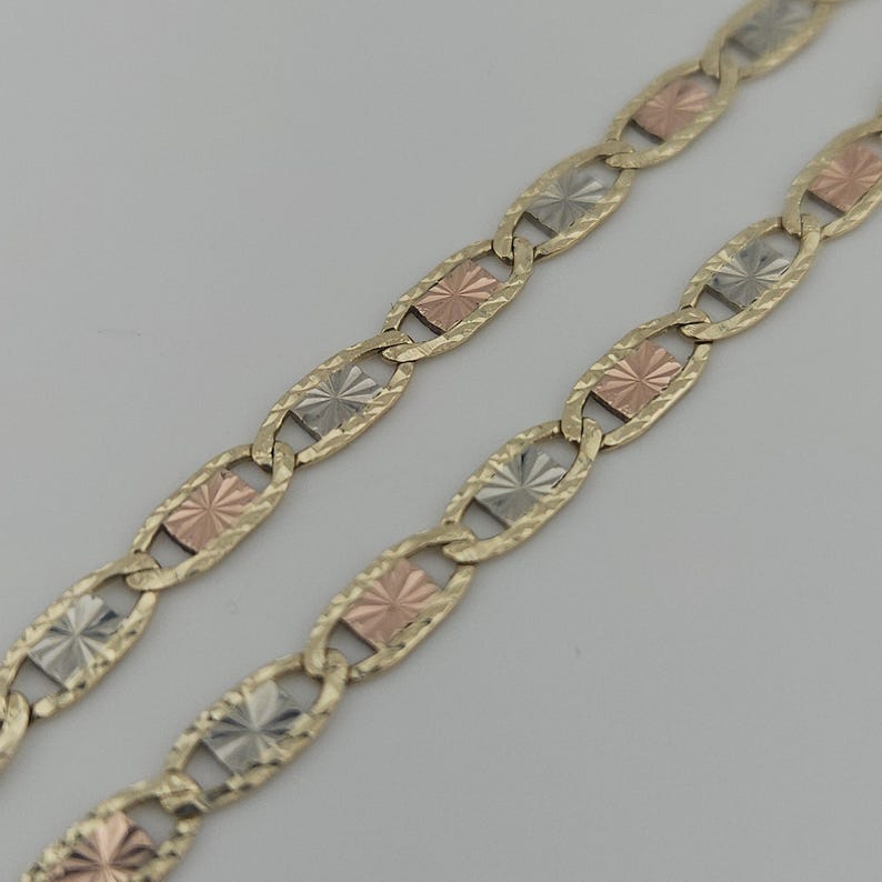 May include: A tri-color chain necklace featuring alternating oval links with a textured finish. The links are connected by small rectangular plates in alternating rose gold, yellow gold, and silver tones, each featuring a sunburst pattern.