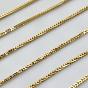 May include: A series of gold-colored wheat chains arranged in parallel diagonal lines. Each chain features a tightly woven, braided metal link pattern that creates a smooth, continuous texture with a reflective, polished finish across the surface.
