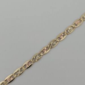 May include: A tri-color gold chain necklace featuring a repeating pattern of elongated oval links. Each link is connected by a smaller, textured square-shaped component that alternates between yellow, rose, and white gold tones with a diamond-cut finish.