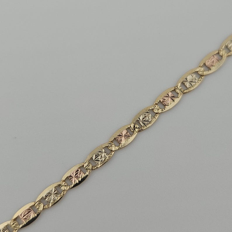 May include: A tri-color gold chain necklace featuring a repeating pattern of elongated oval links. Each link is connected by a smaller, textured square-shaped component that alternates between yellow, rose, and white gold tones with a diamond-cut finish.