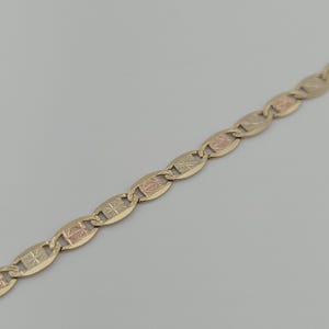 May include: A gold chain necklace featuring a series of repeating oval links. Each link contains a central rectangular panel with a textured, starburst-like etched pattern in a contrasting rose gold tone against the yellow gold frame.