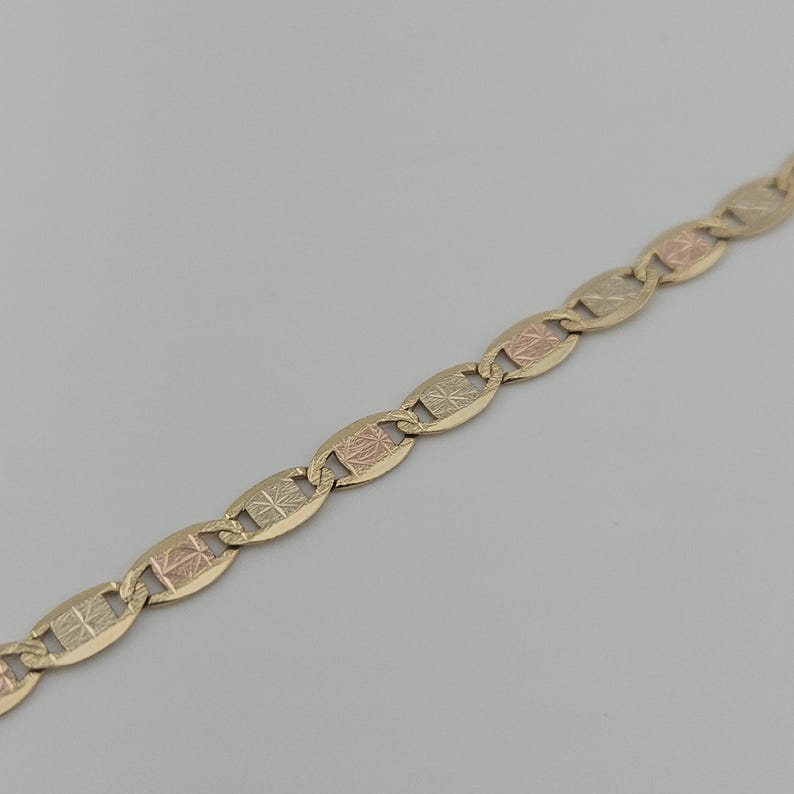 May include: A gold chain necklace featuring a series of repeating oval links. Each link contains a central rectangular panel with a textured, starburst-like etched pattern in a contrasting rose gold tone against the yellow gold frame.