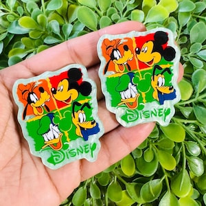 May include: Two square-shaped Disney character charms. Each charm features Mickey Mouse, Goofy, Donald Duck, and Pluto in a colorful grid design. The word "DISNEY" is printed in green at the bottom of each charm.