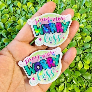 May include: Two stickers with the phrase "Pray More Worry Less" in a colorful design. The stickers have a white border and feature the words in pink, purple, and teal, with a holographic effect on the word "Worry".