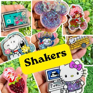 May include: A collection of acrylic shaker charms featuring various characters and designs, including a classroom chalkboard, a mouse-shaped glitter piece, a strawberry-themed character, a dog, a bus, and a cat with a medical ultrasound monitor.