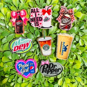 May include: A collection of eight beverage-themed stickers featuring Dr Pepper bottles and cans with bows, a Mountain Dew logo, a Starbucks iced coffee cup, a Dutch Bros cup, a Pepsi Girl heart-shaped sticker, and a Diet Pepper text graphic.