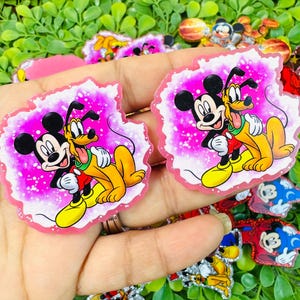 May include: Two Mickey Mouse and Pluto character-themed stickers. The stickers feature Mickey Mouse in a red shirt and Pluto in a yellow body, hugging each other against a pink background with a white border. Other character stickers are visible.