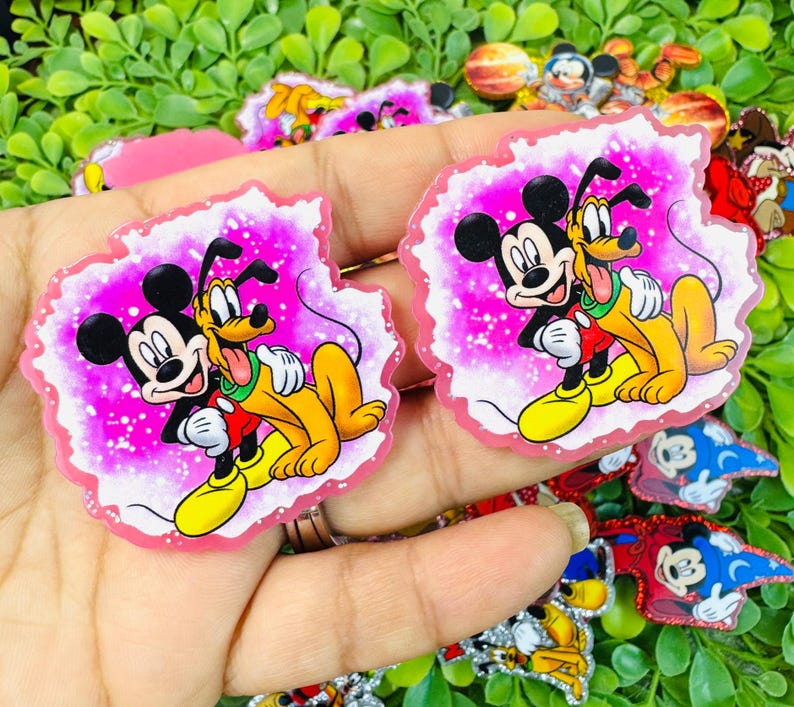 K&ouml;nnte beinhalten: Zwei Aufkleber mit den Figuren Micky Maus und Pluto. Micky Maus tr&auml;gt ein rotes Hemd und Pluto hat einen gelben K&ouml;rper, die sich vor einem rosa Hintergrund mit wei&szlig;em Rand umarmen. Weitere Charakteraufkleber sind sichtbar.