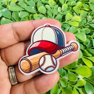 May include: A sticker featuring a white and red baseball cap, a wooden baseball bat with a light brown grain, and a white baseball with red stitching. The design has a thick white border and a cartoon-style illustration with bold outlines.