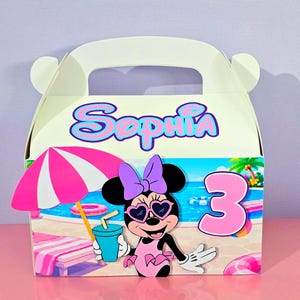 May include: A white party favor box with a handle, featuring a Minnie Mouse design. The box has a beach scene with a pink umbrella, a number 3, and the name "Sophia" in blue and pink. Minnie Mouse is wearing sunglasses and a swimsuit.